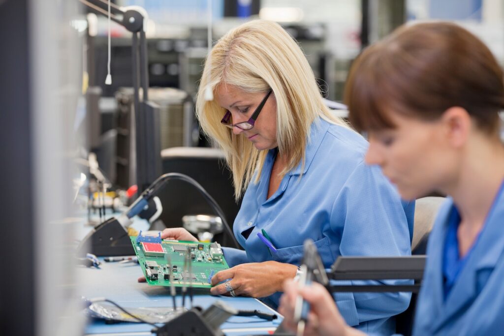 Female technician at a workbench working on PCB design and assembly integration.