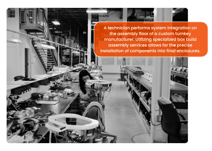 A technician performs system integration on the assembly floor of a custom turnkey manufacturer. Utilizing specialized box build assembly services allows for the precise installation of components into final enclosures.]