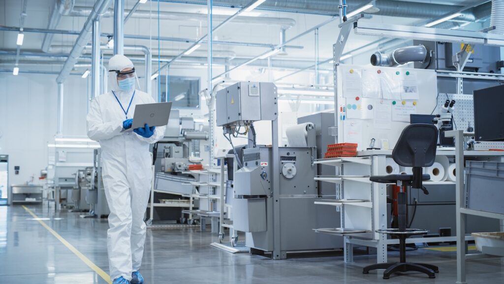 Person reviewing medical device engineering data on human factors while walking in a manufacturing facility and consulting with another engineer.